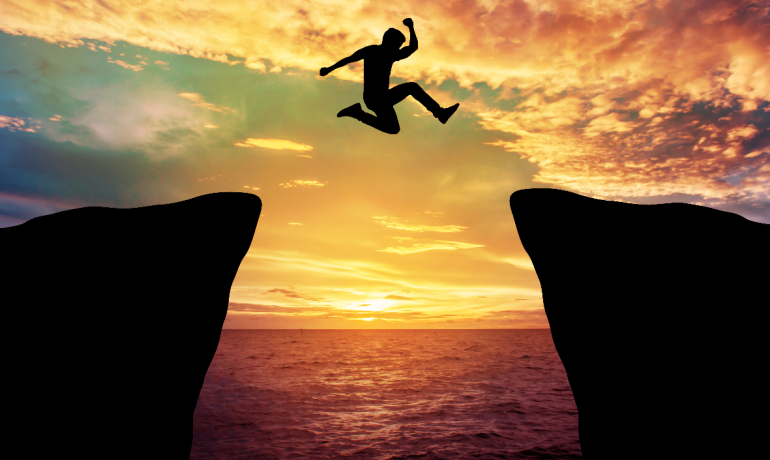 A man jumping over cliff with sunset in background